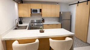 Een moderne keuken met een centraal eiland, twee barkrukken, een magnetron, een fornuis en een koelkast.