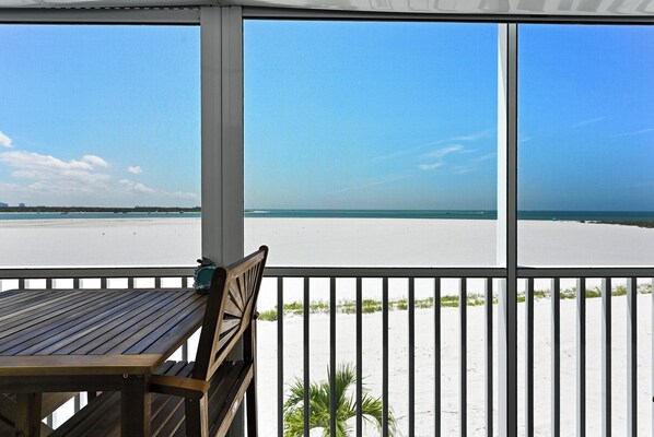 Ein Holztisch und ein Stuhl auf einem Balkon mit Blick auf Strand und Meer.