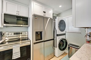 Una cocina equipada con electrodomésticos de acero inoxidable, horno empotrado, microondas, refrigerador y lavadora.