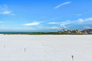 Ein Strand mit weißem Sand, blauem Himmel und einer Reihe von Gebäuden im Hintergrund.