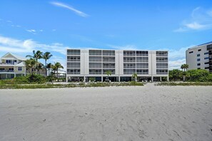 Un hotel frente a la playa con varios pisos, balcones y una playa arenosa al frente.