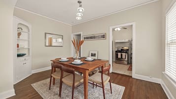 A dining area with a wooden table, four chairs, a rug, a ceiling light fixture, a white cabinet, and a framed picture on the wall.