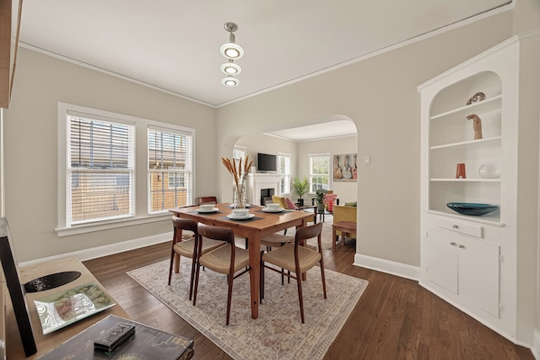 A dining area with a wooden table, chairs, and a rug. There is a white cabinet with shelves and a television in the background. - Colorful Stylish Museum & Med District + Parking (Houston)