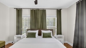 Een slaapkamer met een groot bed, twee nachtkastjes, een raam met gordijnen.