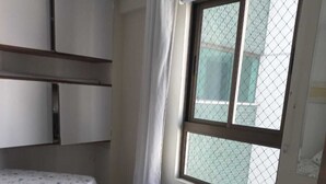 Een slaapkamer met een bed, een raam met gordijn en een betegelde vloer.