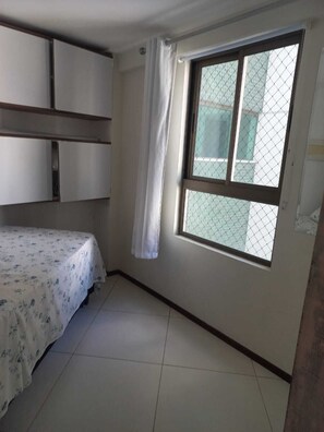 Ein Schlafzimmer mit einem Bett, einem Fenster mit Vorhang und einem Fliesenboden.