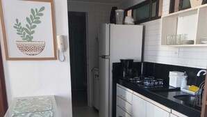 Een compacte keuken met witte kastjes, een zwart aanrecht en een klein zithoekje met een tafel en krukje.