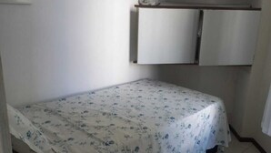 Een kleine kamer met een enkel bed, een kledingkast en een wandplank.