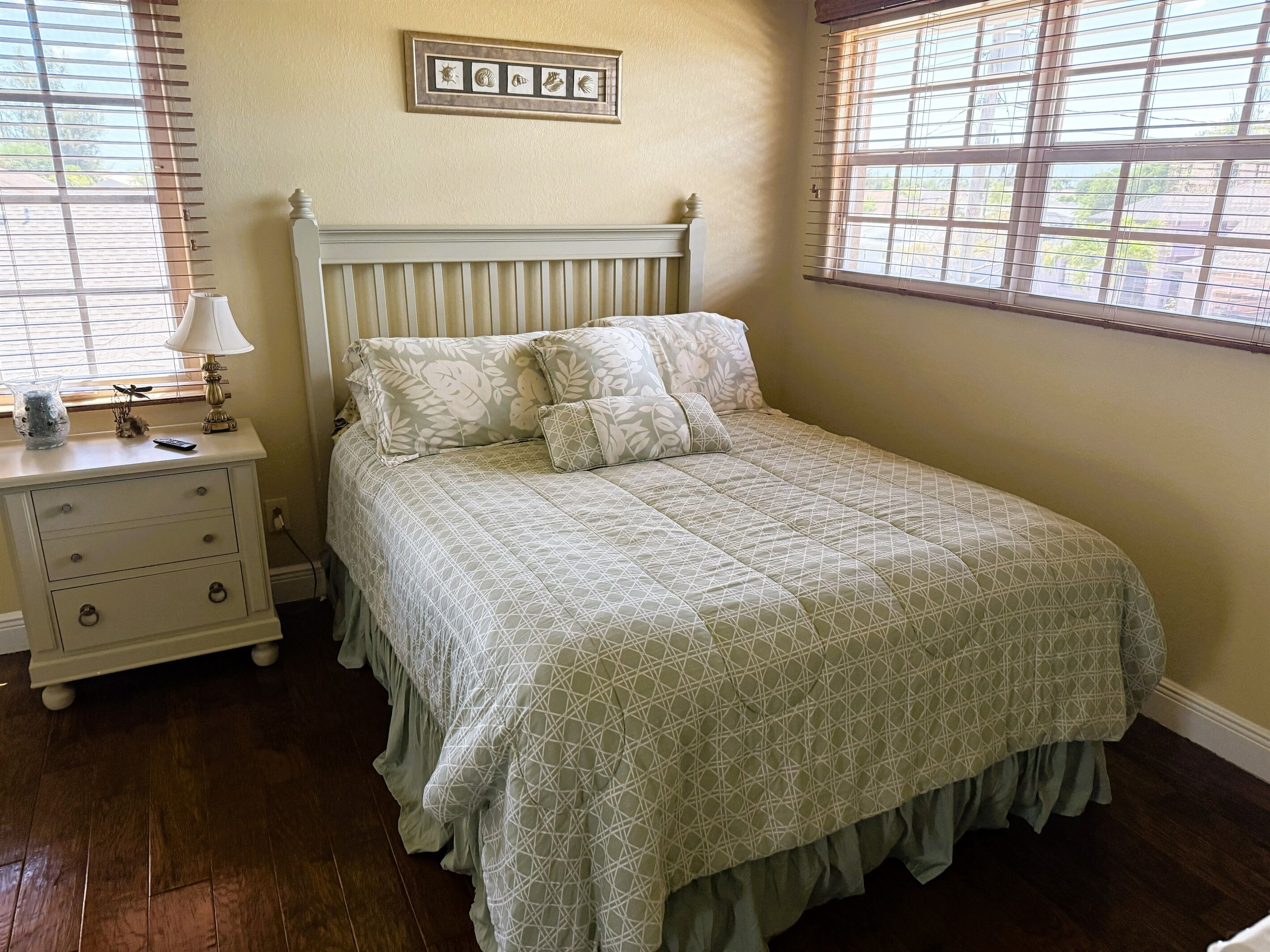 A bedroom with a bed, a nightstand, a lamp, and a window with blinds.