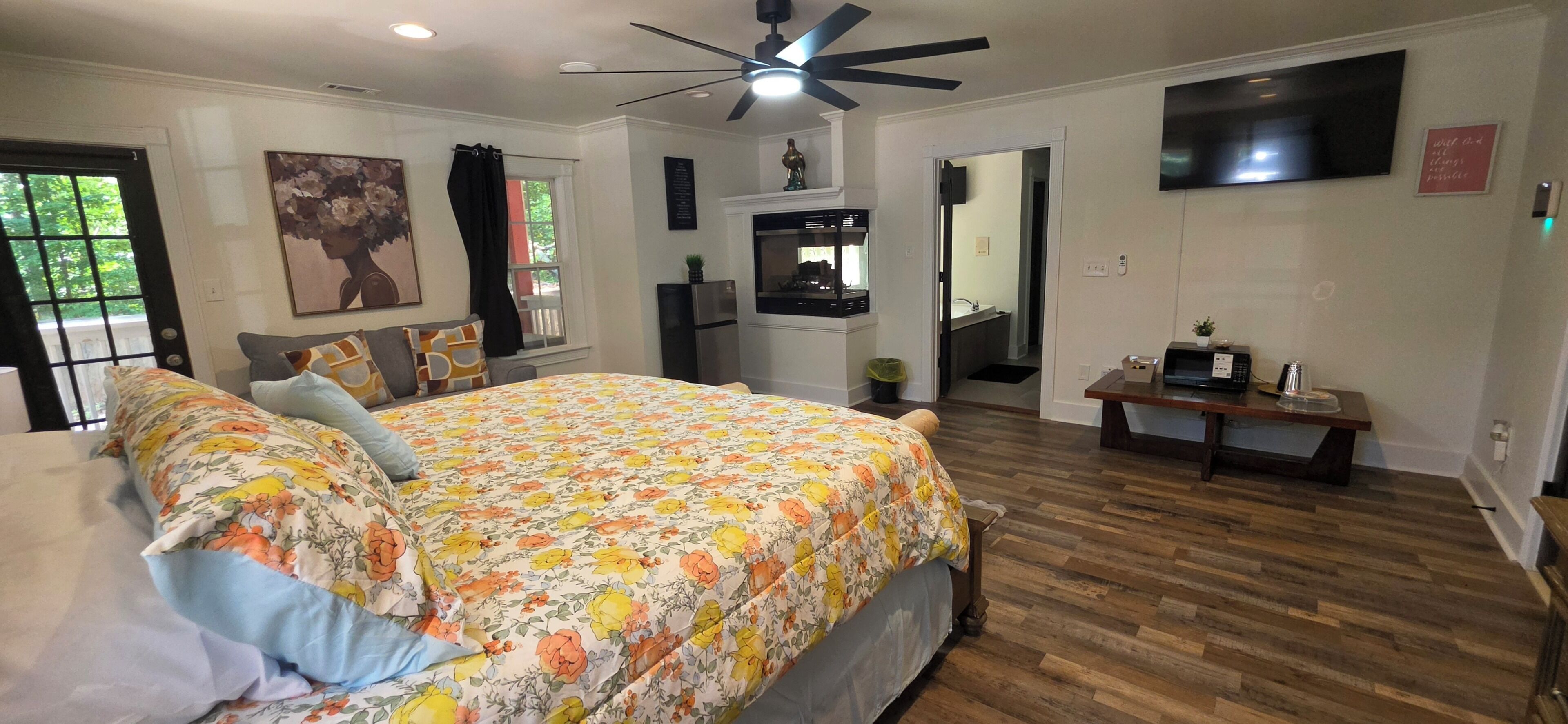 A bedroom with a bed, a ceiling fan, a TV, and a wooden floor.