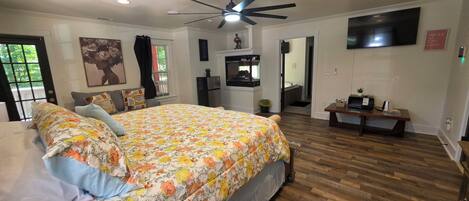 A bedroom with a bed, a ceiling fan, a TV, and a wooden floor.