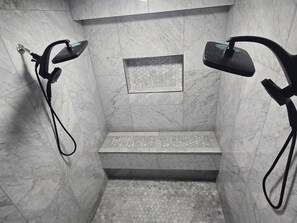 A shower with a marble wall, a small shelf, and a hexagonal tile pattern on the floor. - Beautiful 3-bedroom bed & breakfast in enjoyable Covington with AC (Covington)