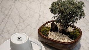Duas chávenas de cerâmica branca com um logótipo sobre uma superfície de mármore, acompanhadas por uma pequena árvore bonsai num vaso castanho.
