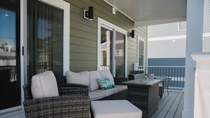A covered outdoor seating area with wicker furniture, a glass door, and a view of the ocean. - 4BR oceanfront-area condo with balcony, arcade bunk room, and outdoor firepit (Virginia Beach)