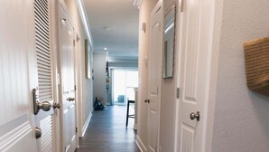 A hallway with white doors and a wooden floor. - 4BR oceanfront-area condo with balcony, arcade bunk room, and outdoor firepit (Virginia Beach)
