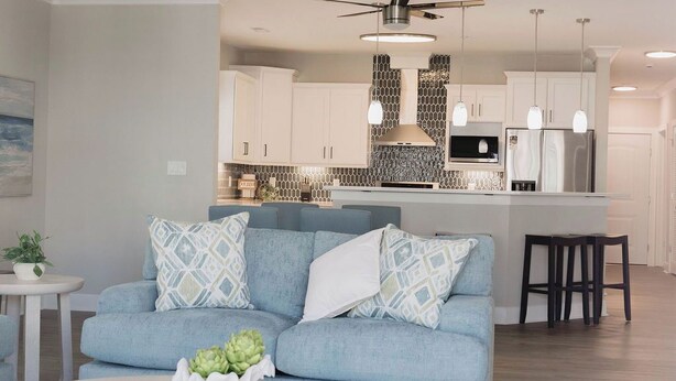 A modern living room with a sofa, coffee table, and a kitchen in the background. - 4BR oceanfront-area condo with balcony, arcade bunk room, and outdoor firepit (Virginia Beach)