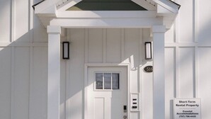 A white building with a front door, a small porch, and a sign indicating short-term rental property. - 4BR oceanfront-area condo with balcony, arcade bunk room, and outdoor firepit (Virginia Beach)