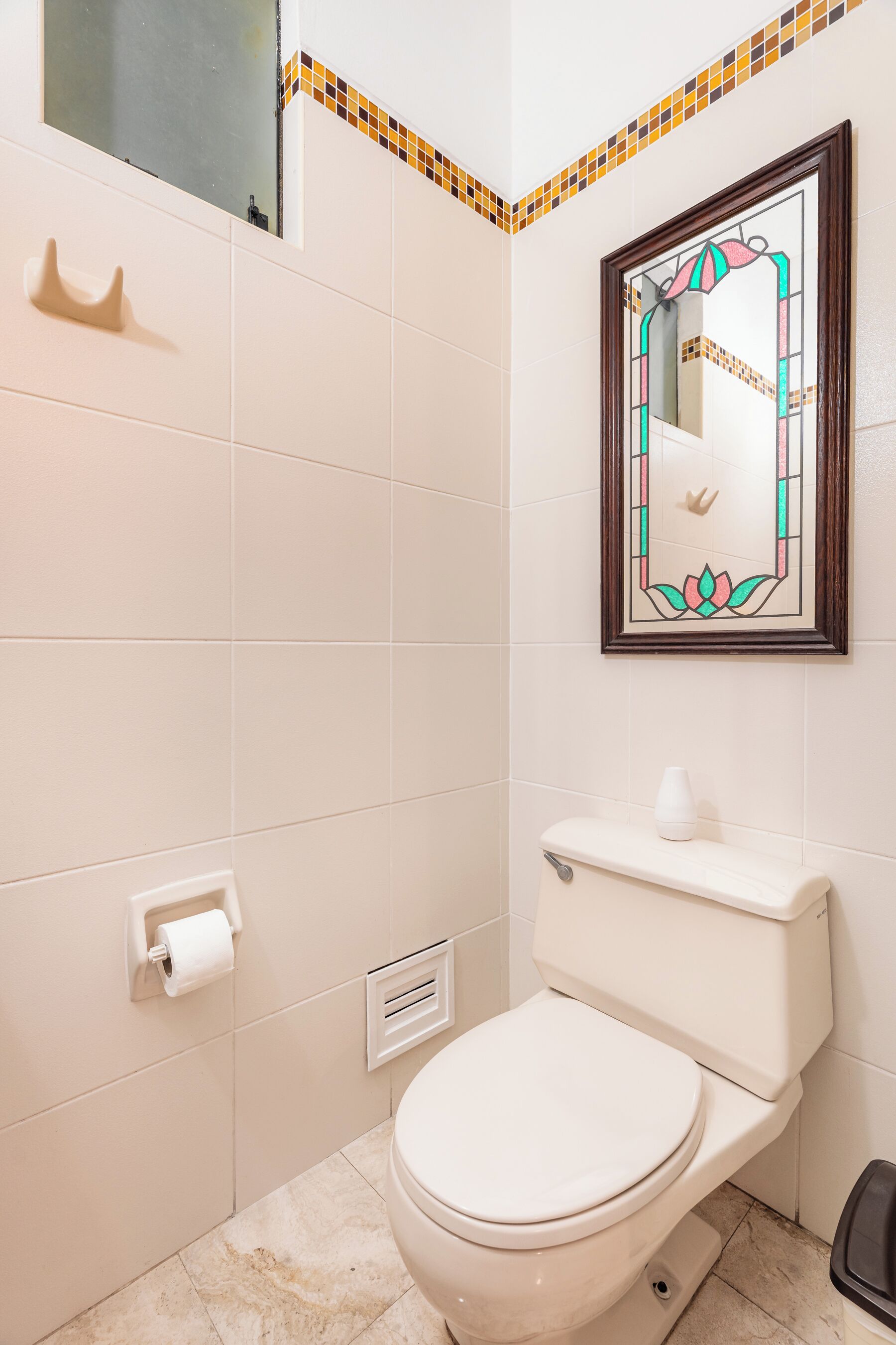Et badeværelse med toilet, hårtørrer, spejl med dekorativ ramme og toiletpapirsholder.