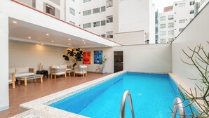 Ein Pool auf dem Dach mit gefliestem Rand, Liegestühlen und einer Wand mit Kunstwerken.
