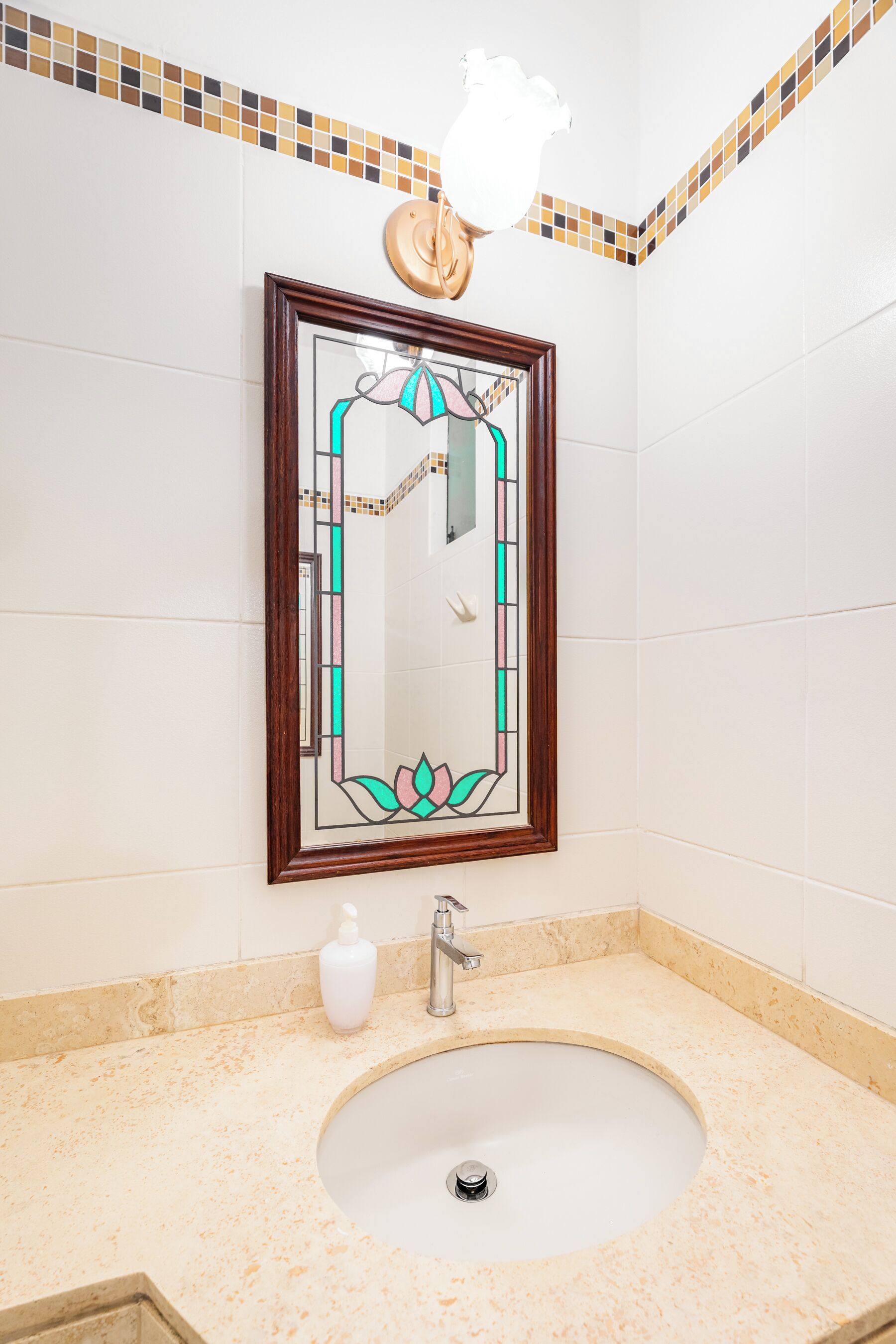 Une salle de bain avec un lavabo blanc, un miroir encadré, un distributeur de savon et un luminaire fixé au mur.