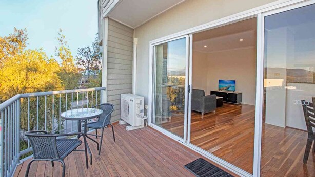 Un balcon avec une table et des chaises, une porte-fenêtre coulissante donnant sur un espace de vie comprenant un canapé et un téléviseur.