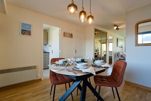 A dining area with a table set for four, chairs, and hanging pendant lights. - Souvenirs de Mer - À 300 m de la mer (Courseulles-sur-Mer)