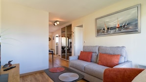 Ein Wohnzimmer mit grauem Sofa, roten Kissen, einem Segelboot-Bild, einem Holztisch und einer Pflanze.
