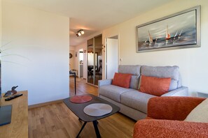 Ein Wohnzimmer mit grauem Sofa, roten Kissen, einem Segelboot-Bild, einem Holztisch und einer Pflanze.