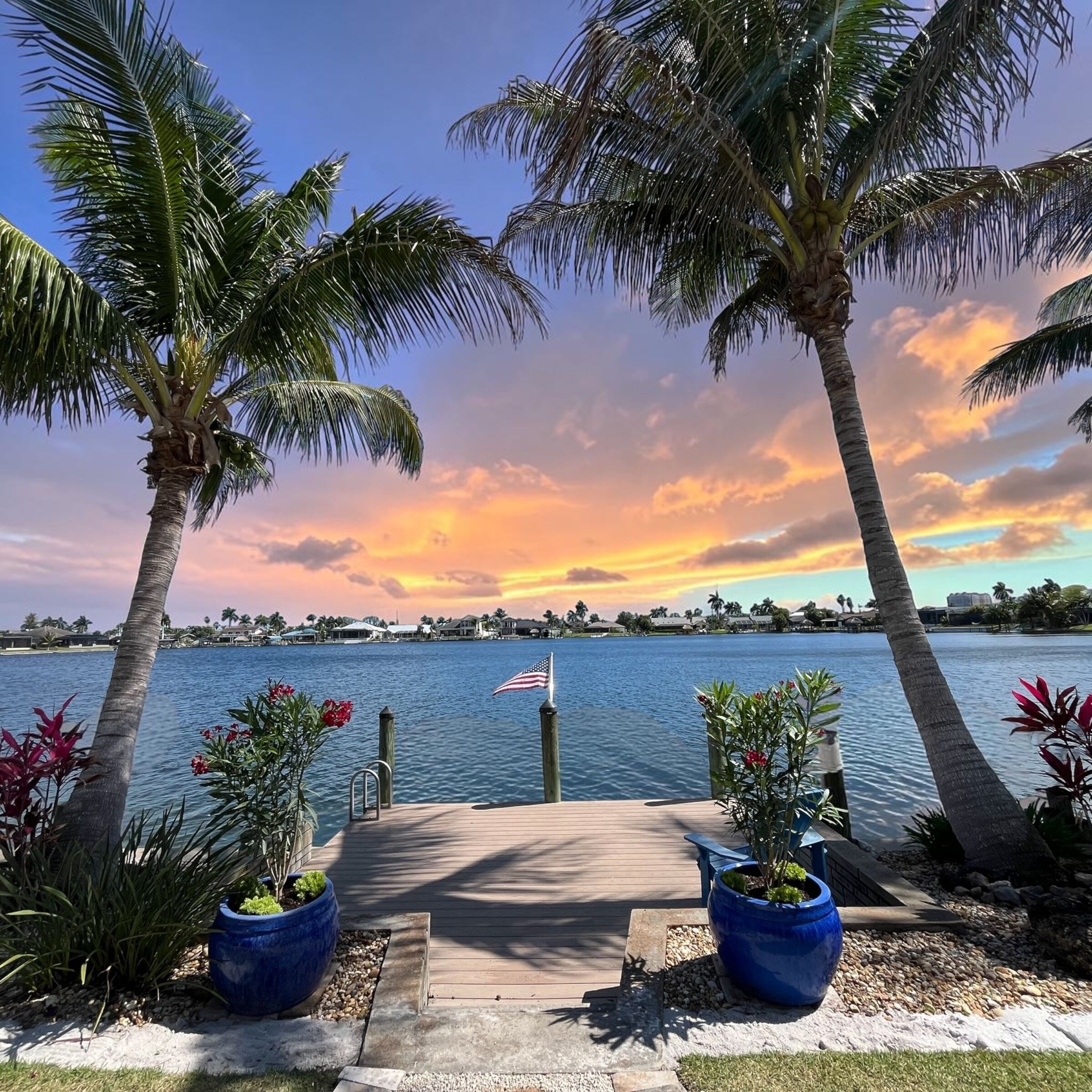 A waterfront view with palm trees, a dock, and a flag.