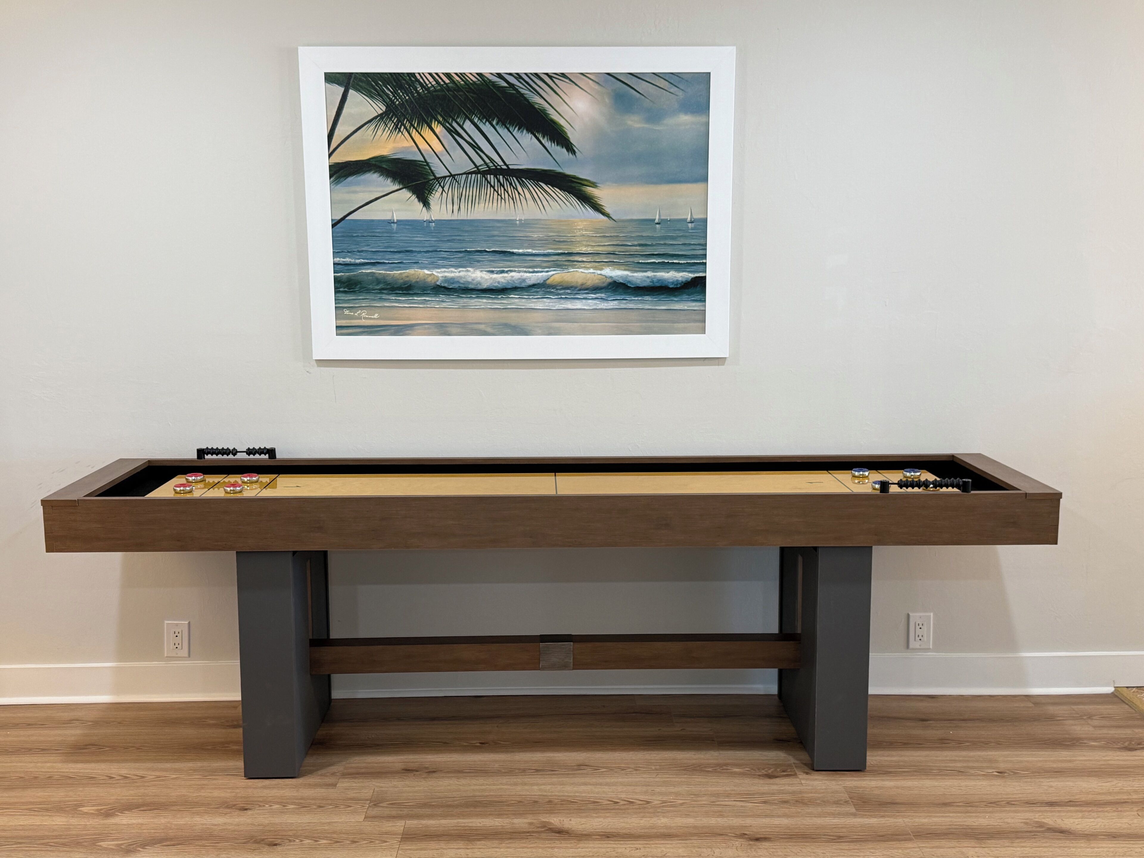 Une table de baby-foot surmontée d’un tableau encadré représentant une scène de plage.