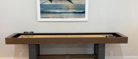 Une table de baby-foot surmontée d’un tableau encadré représentant une scène de plage.