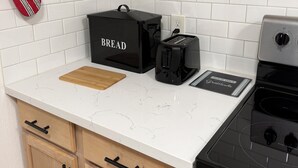 Eine Küche mit weiß gefliestem Spritzschutz, Holzschränken, einer schwarzen Brokkiste, einem Toaster und einem Herd.