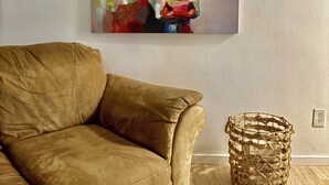 Ein braunes Ledersofa, ein gewebter Korb und ein farbenfrohes abstraktes Gemälde einer Kuh an der Wand.
