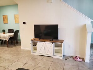 A living room with a TV on a wooden stand, a dining table with chairs, and a staircase. - 3-bedroom townhome in fantastic Davenport (Davenport)
