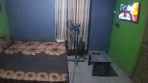 Una habitación con cama, ventilador, televisor y una mesita.