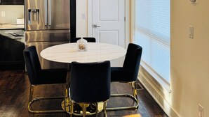 Une cuisine moderne avec un réfrigérateur en acier inoxydable, une table à manger avec des chaises noires et une fenêtre équipée de stores.