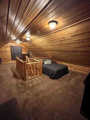 A cozy attic bedroom with a wooden ceiling, a bunk bed, and a small wooden staircase. - Cozy 3-bedroom house with lake access on beautiful Otsego Lake! (Gaylord)