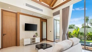 Uma sala de estar moderna com televisão de tela plana, um sofá, uma mesa de centro e uma porta de vidro deslizante que dá para uma varanda.
