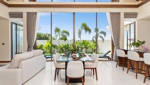 Uma sala de jantar ampla, com uma mesa grande, cadeiras e vista para um jardim tropical.