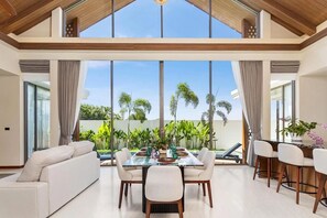 A spacious dining area with a large table, chairs, and a view of a tropical garden. - The Ozone Pool Villas by NLA (Choeng Thale)