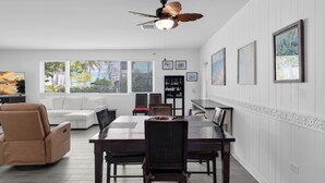 A spacious living area with a dining table, reclining chairs, a ceiling fan, and framed artwork on the walls. - Surf Shack - Downtown Islamorada 2 Bedroom Beach Bungalow (Islamorada)