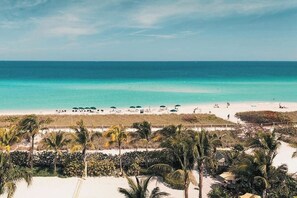 A beach with clear turquoise water, palm trees, and a few umbrellas. - Cozy 1-bedroom condo in brilliant Surfside with AC and gym access (Surfside)