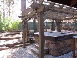 A covered outdoor seating area with a stone fireplace, wooden steps, and a pergola with string lights. - 3 Bedroom, 2 Bath w/Spa & Gameroom, Walk to Park & Lake 1/2 mile to Ski/Shopping (Big Bear Lake)