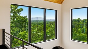 Ein Zimmer mit großen Fenstern und Blick auf ein bewaldetes Gebiet und Berge.