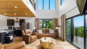 Ein modernes Wohnzimmer mit Ledermöbeln, einem Holztisch und einer Küche im Hintergrund.