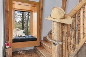 Eine Holztreppe im rustikalen Stil, eine Fensterbank mit Kissen und ein Cowboyhut auf der Geländer.