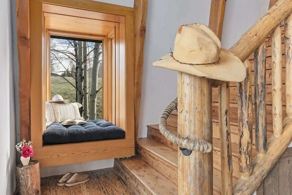 Una scala in legno dal design rustico, una panchina finestrata con un cuscino e un cappello da cowboy sulla ringhiera.