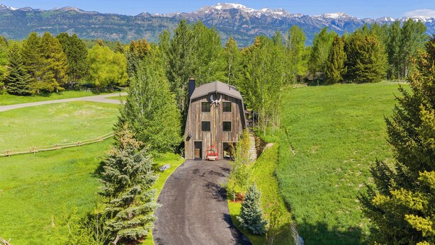 A wooden cabin with a sloped roof, surrounded by a green landscape and mountains in the background. - Abode at Luxe Barnhouse, teton views, hot tub (Jackson)