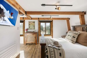 Ein Schlafzimmer mit Holzbalkendecke, einem Bett mit gemusterten Textilien, einer Bank, einem Hut und einem Bild eines Skifahrers.
