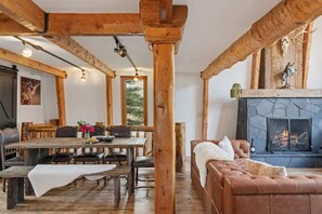 Un intérieur rustique avec des poutres apparentes, une cheminée, un coin repas et un canapé en cuir.
